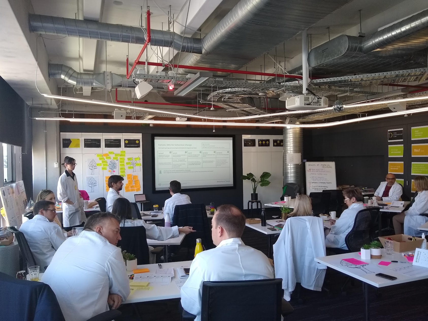 People taking part in a Behavioural Science Lab workshop around tables with behavioural design canvases and sticky notes.