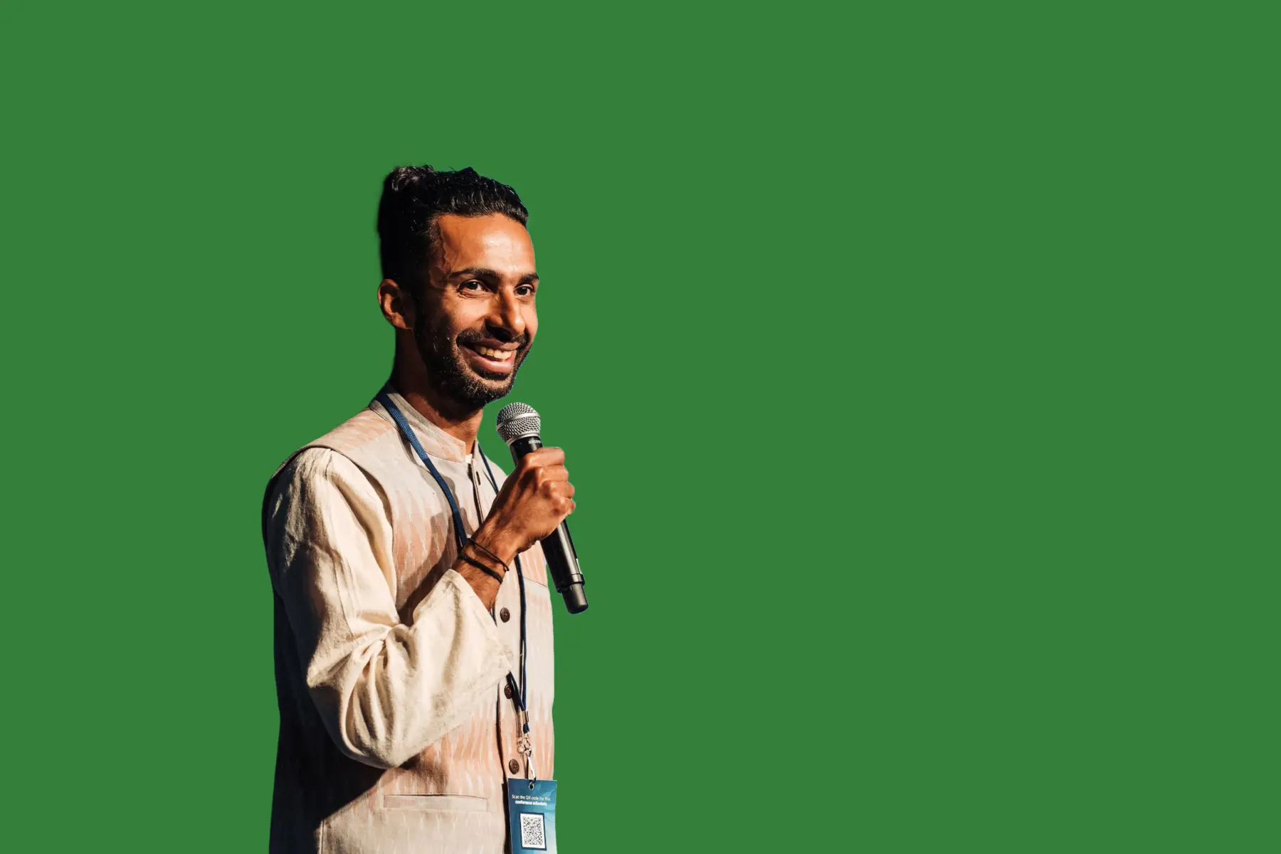 Vishal George mid-speech holding a microphone, on a plain green background.